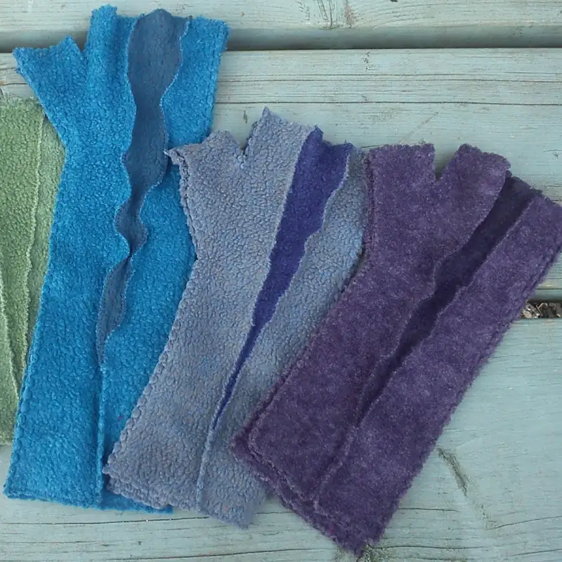 3 pairs of insert Feelne mittens in blues, greys, and soft purples, against a pale turquoise wooden background