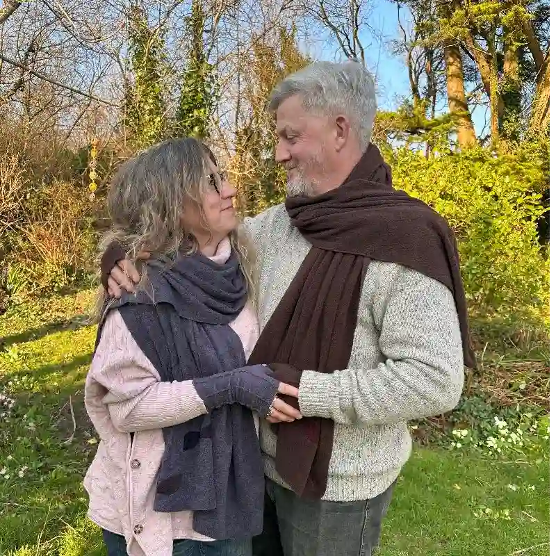 an embracing couple wearing Feeline Clothing scarves and mittens, soft purple/grey pen brown, in a garden setting