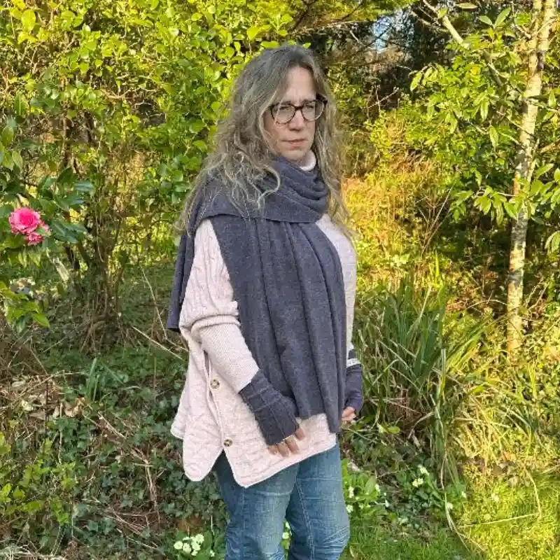 a Feeline Clothing purple/grey wrap/scarf and mittens set being worn in a garden setting
