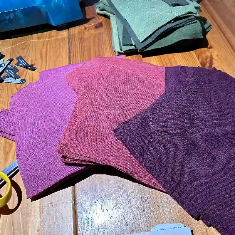 Feeline Clothing work table, piles cut out mittens in shades of pink, cool, and burgundy