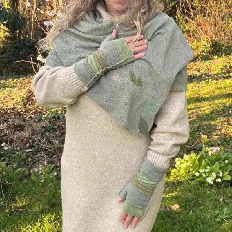 Feeline Clothing striped mittens and scarf/shawl in soft pale shades of greens worn by a woman in a long cream jumper dress in a garden setting