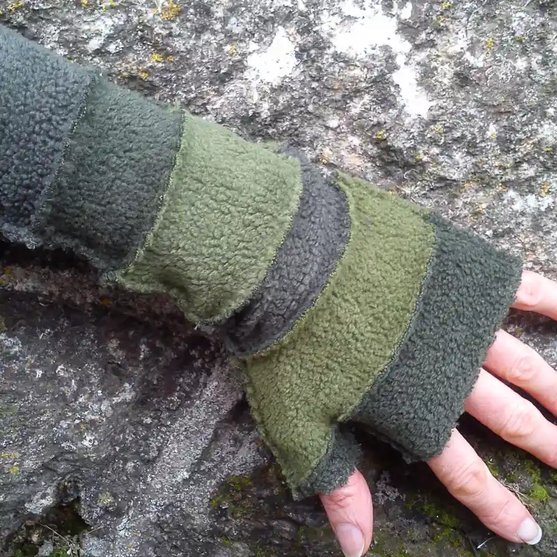 Feeline stripey mitten in shades of green, modelled against a stone wall