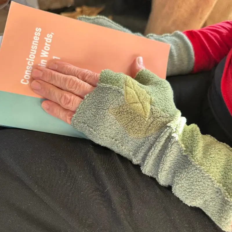 hands wearing soft green mittens with an appliquéd design, holding a book
