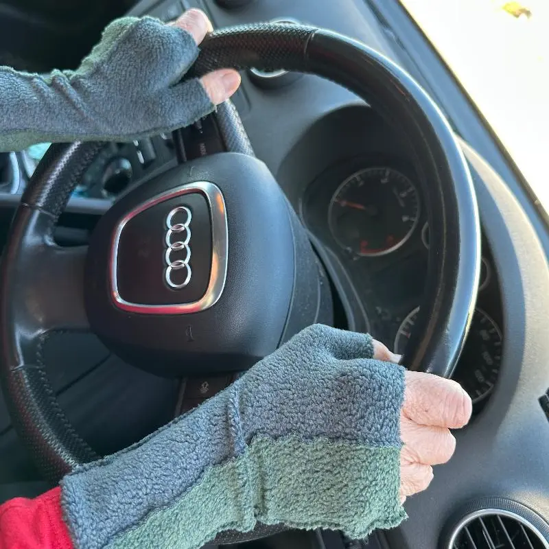 hands wearing two toe soft dull blue grey mittens holding a steering wheel