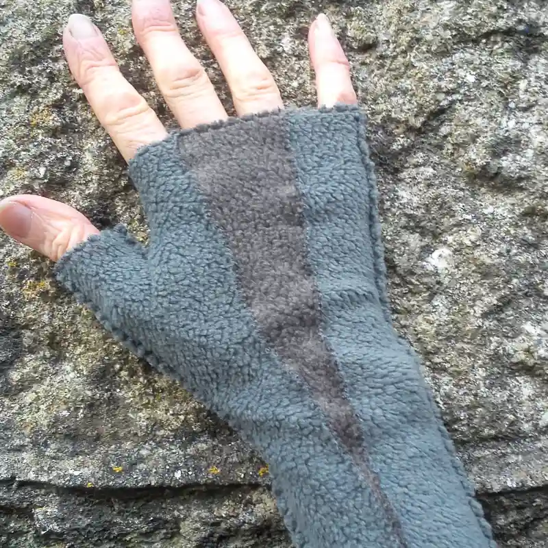 A Feeline Clothing insert mitten, in a blue grey and grey colour way. Modelled against a stone wall background