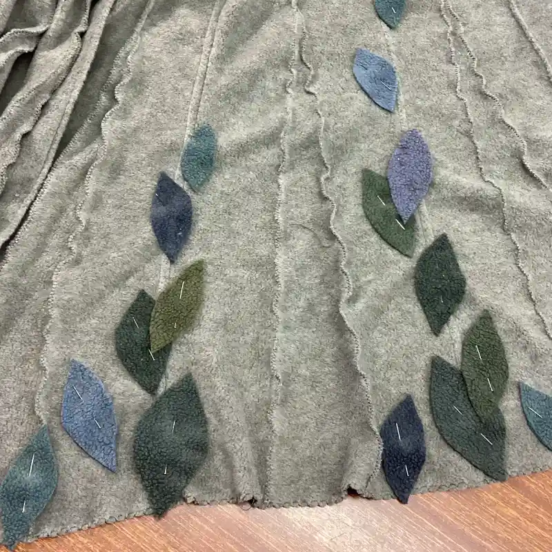 detail of leaves in shades o blue, grey and aqua, pinned onto a Feeline Clothing jacket, ready to be appliquéd on to the soft neutral background.