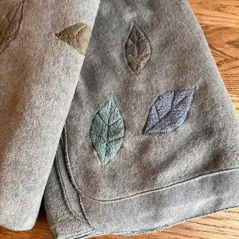 close up detail of leaves, appliquéd onto Feeline Clothing scarves/shawls. In soft muted colours, greys, fawns, green