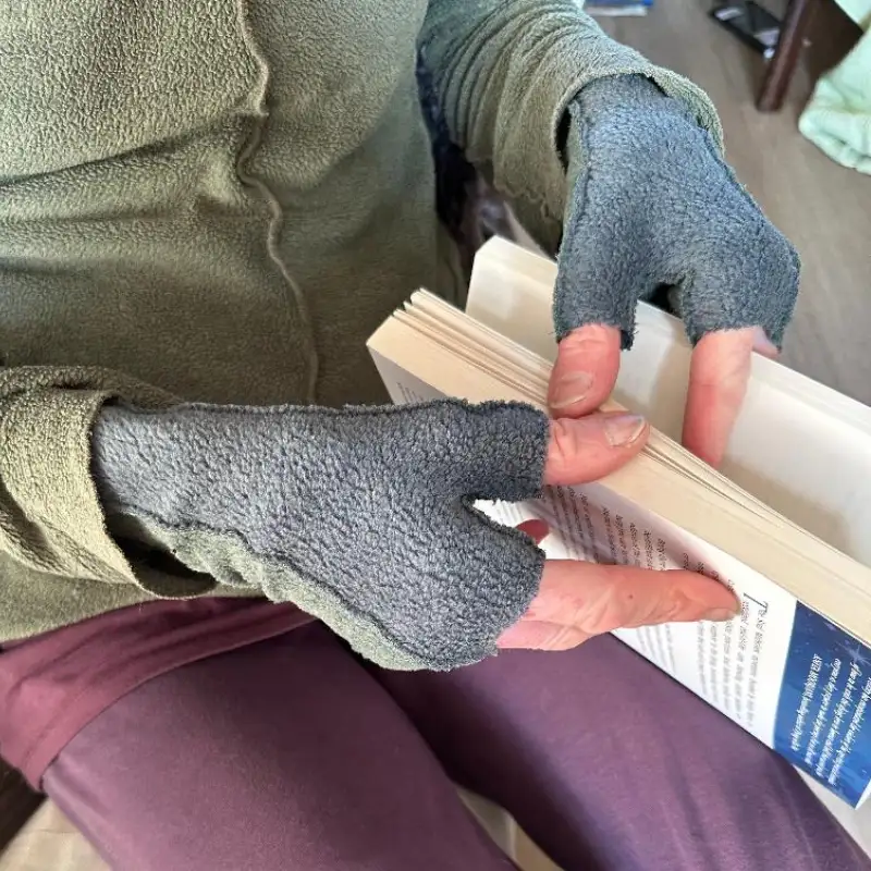 hands wearing soft dark green grey mittens opening a book